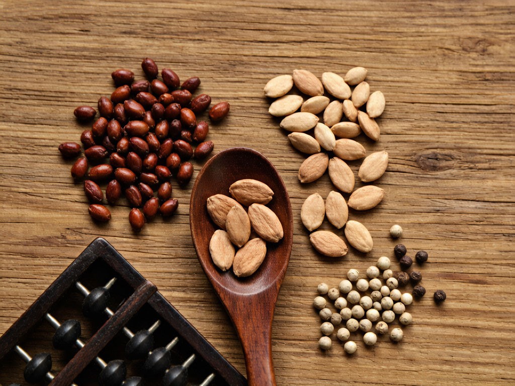 Traditional herbal ingredients including gardenia berries peach kernels apricot seeds and white peppercorns on wooden surface